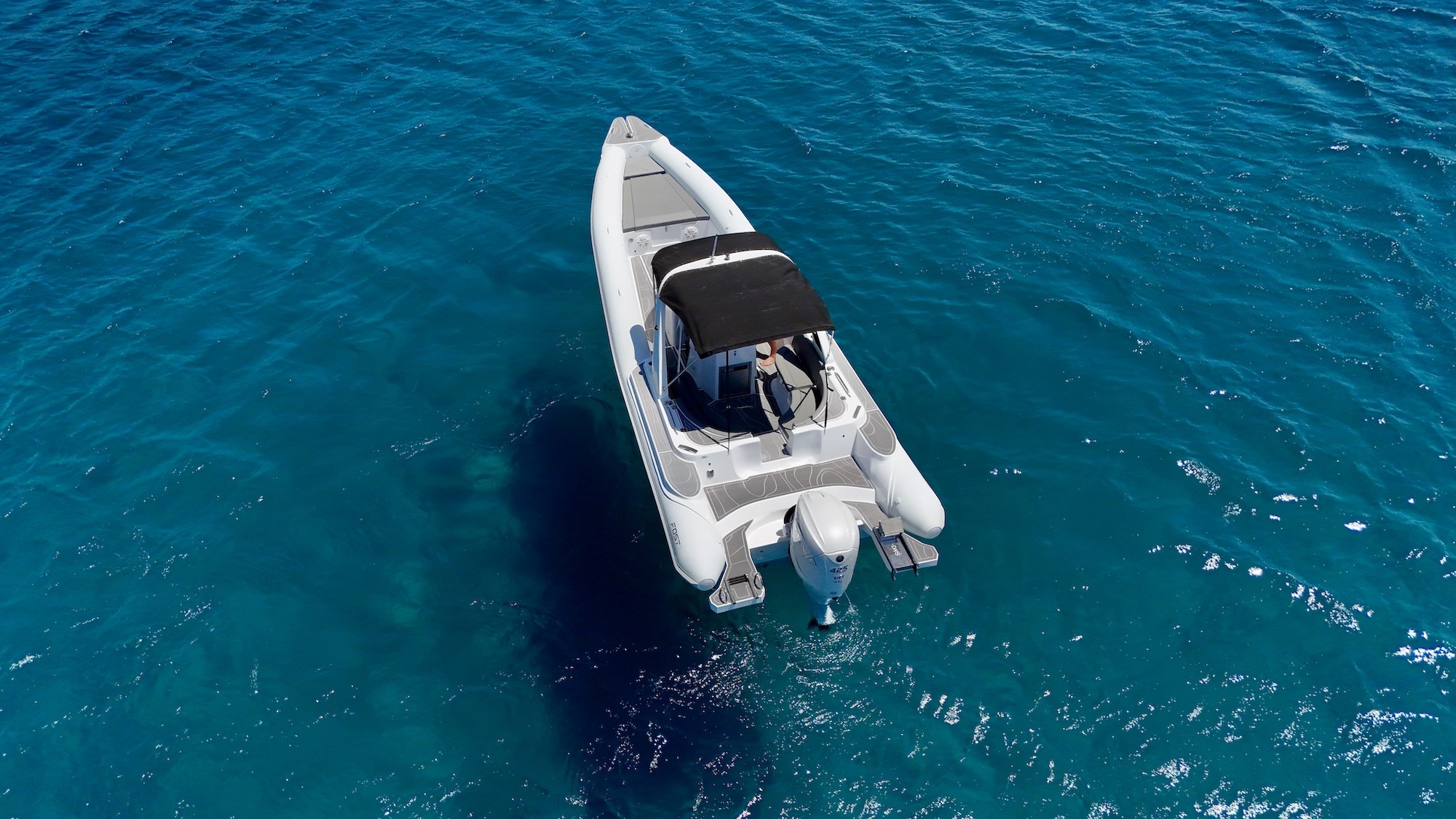 White Fost Matrix 32 speedboat with black T-top canopy anchored in crystal-clear turquoise waters of the Aegean Sea.