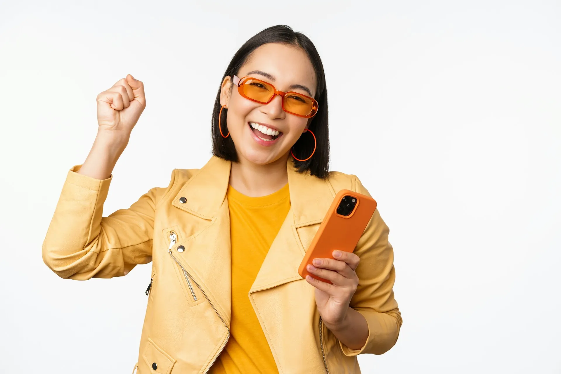 Smiling woman wearing yellow jacket and orange glasses holding a smartphone, illustrating mobile browsing experience and user engagement.