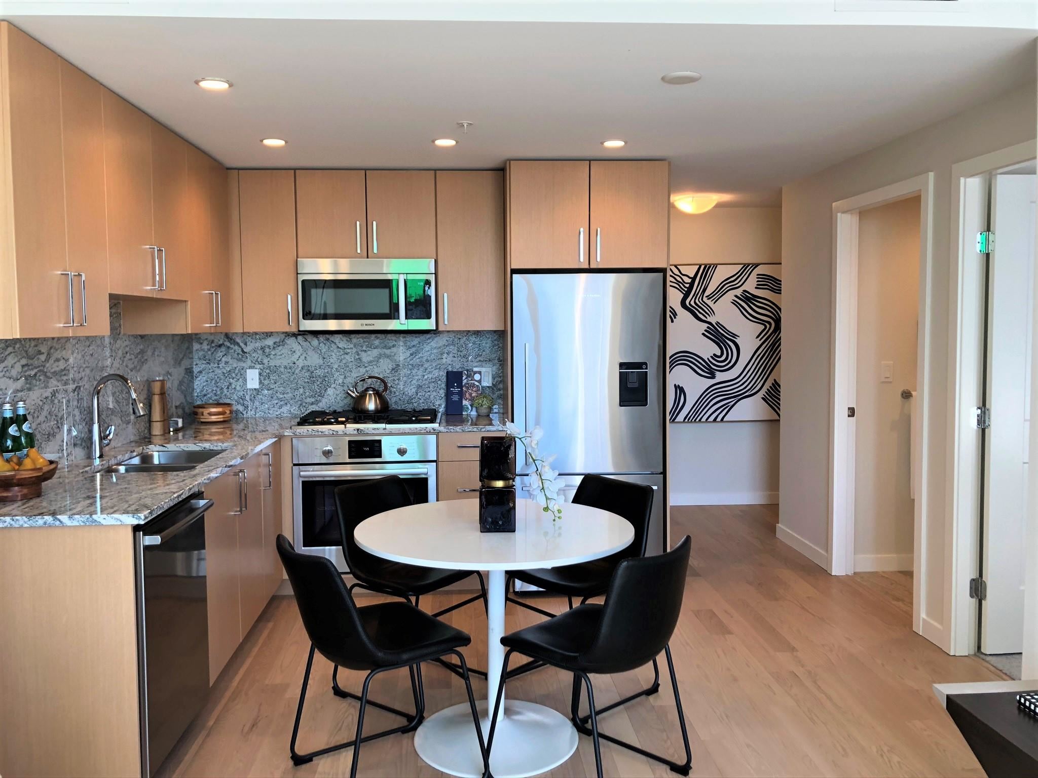 A modern kitchen with wooden cabinets, stainless steel appliances, and a round dining table with black chairs.