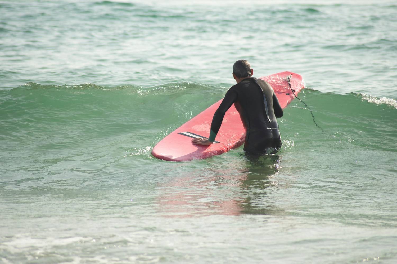 Surfer carrying a pink longboard on a scenic coastal beach — surfboard rental in Europe