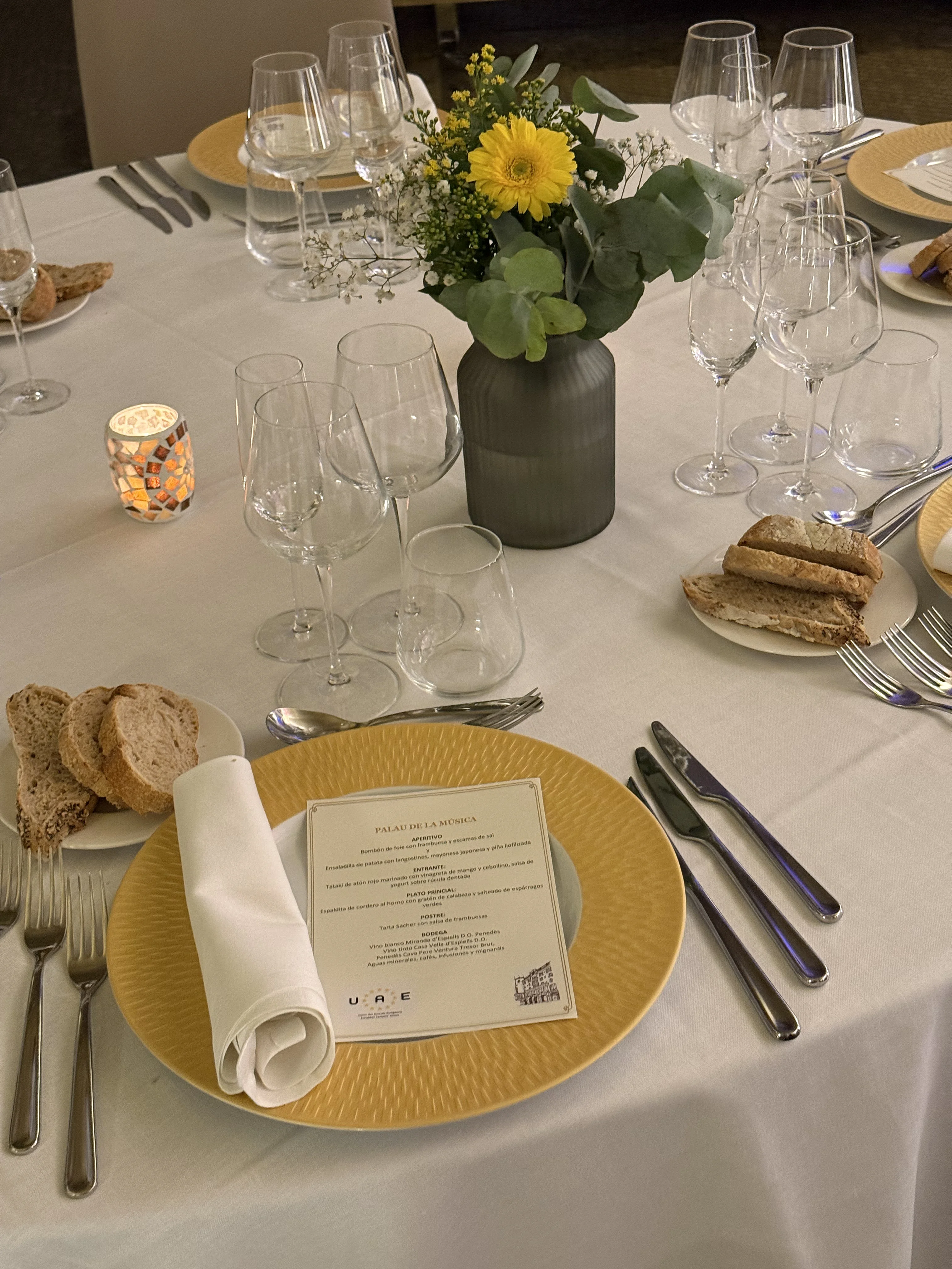 Dinner place setting with a printed menu, yellow charger plate and floral centrepiece