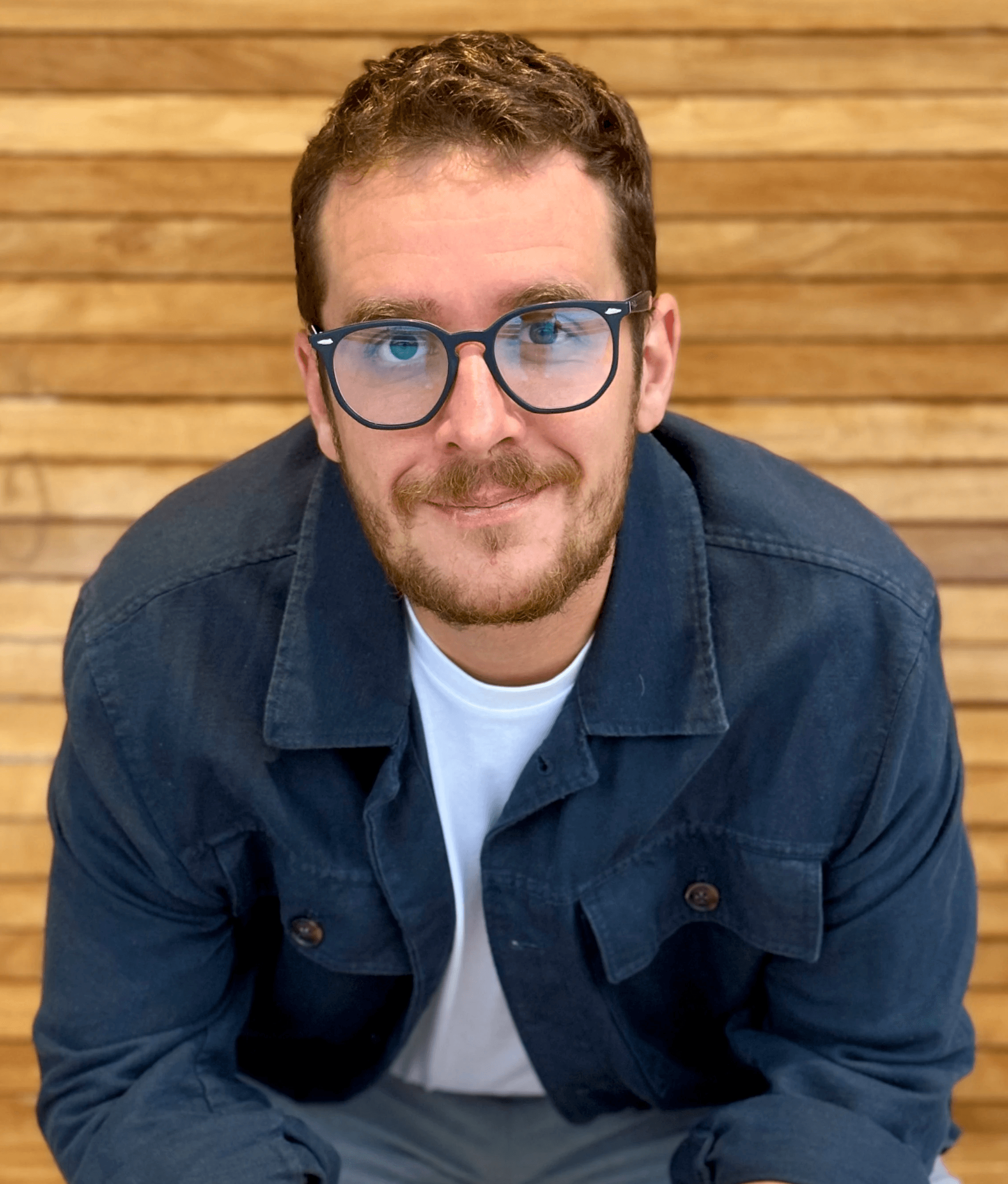A confident person with short, styled hair and a leather jacket poses against a dark backdrop.