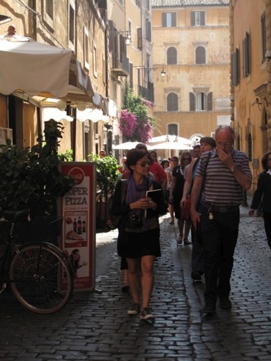 A group of people walking a narrow stone paved street in Rome.