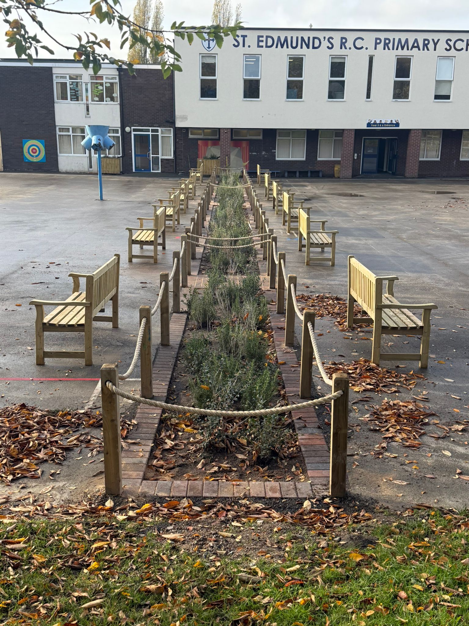 A garden with wooden benches and a wooden trellis surrounded by gravel, set against a building in the background.