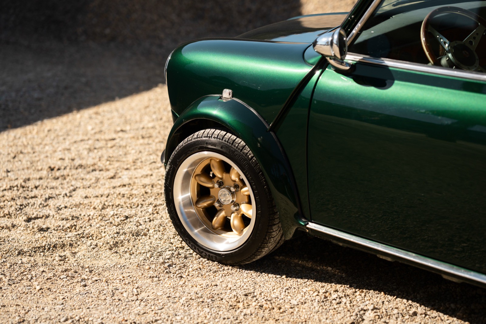 A small, green and black vehicle parked on a sandy surface, with a warm sunset lighting the scene.
