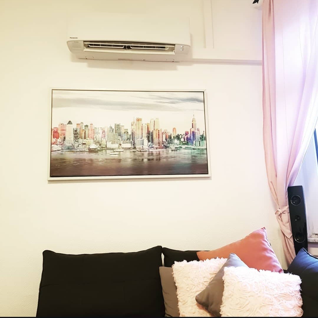 Weißes Klimaanlagen-Wandgerät in einem Wohnraum über einem modernen Stadtbild-Gemälde.