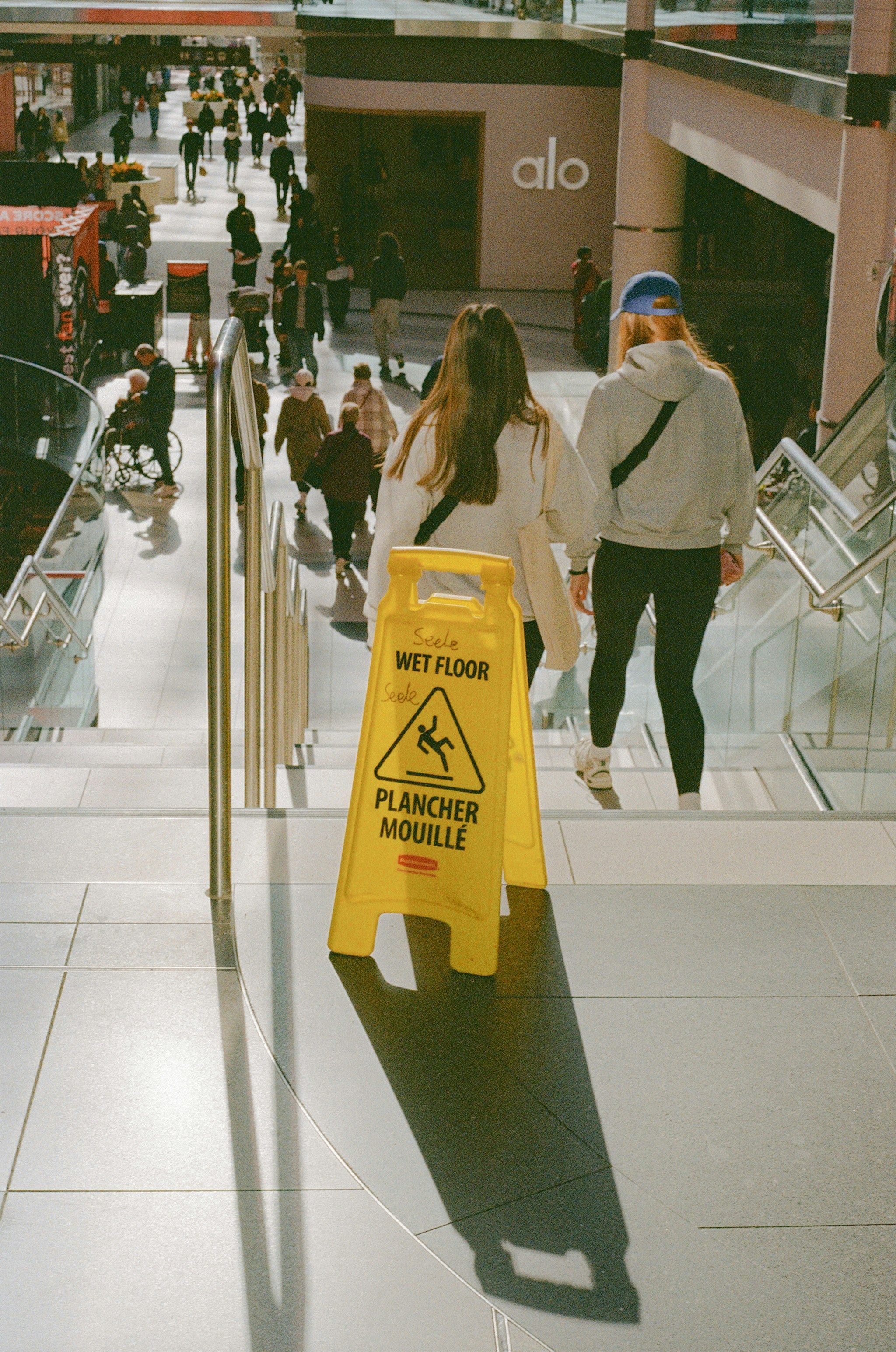 Two people walk up stairs past a wet floor sign.