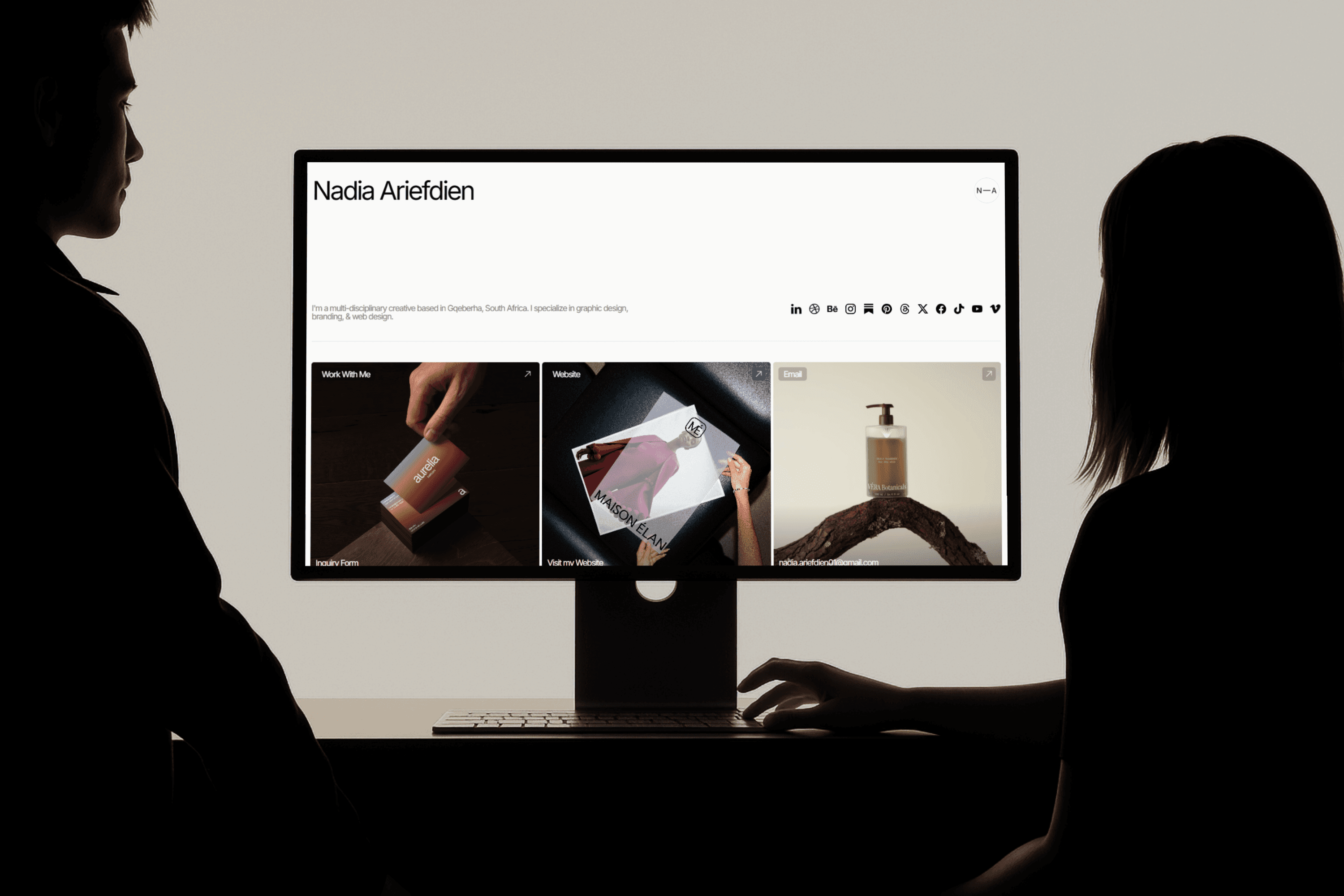 Two people looking at a desktop computer monitor. The screen shows Nadia Ariefdien's link in bio website.