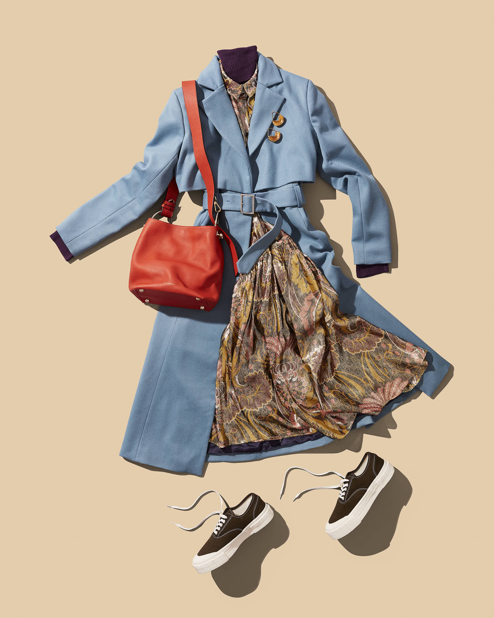 Stylish fall outfit with a blue coat, patterned dress, red handbag, and sneakers on a beige background.