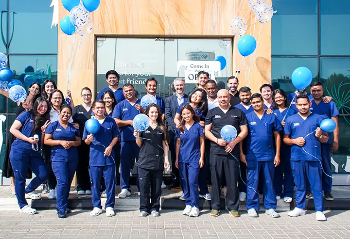 Noble Veterinary Clinics team in blue and black scrubs posing with blue balloons outside a clinic entrance.