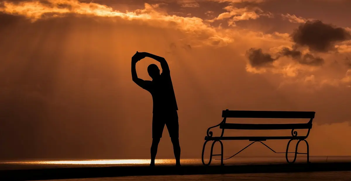 Silhouette of a person stretching at sunrise beside a bench, symbolizing healing, movement, and hope.