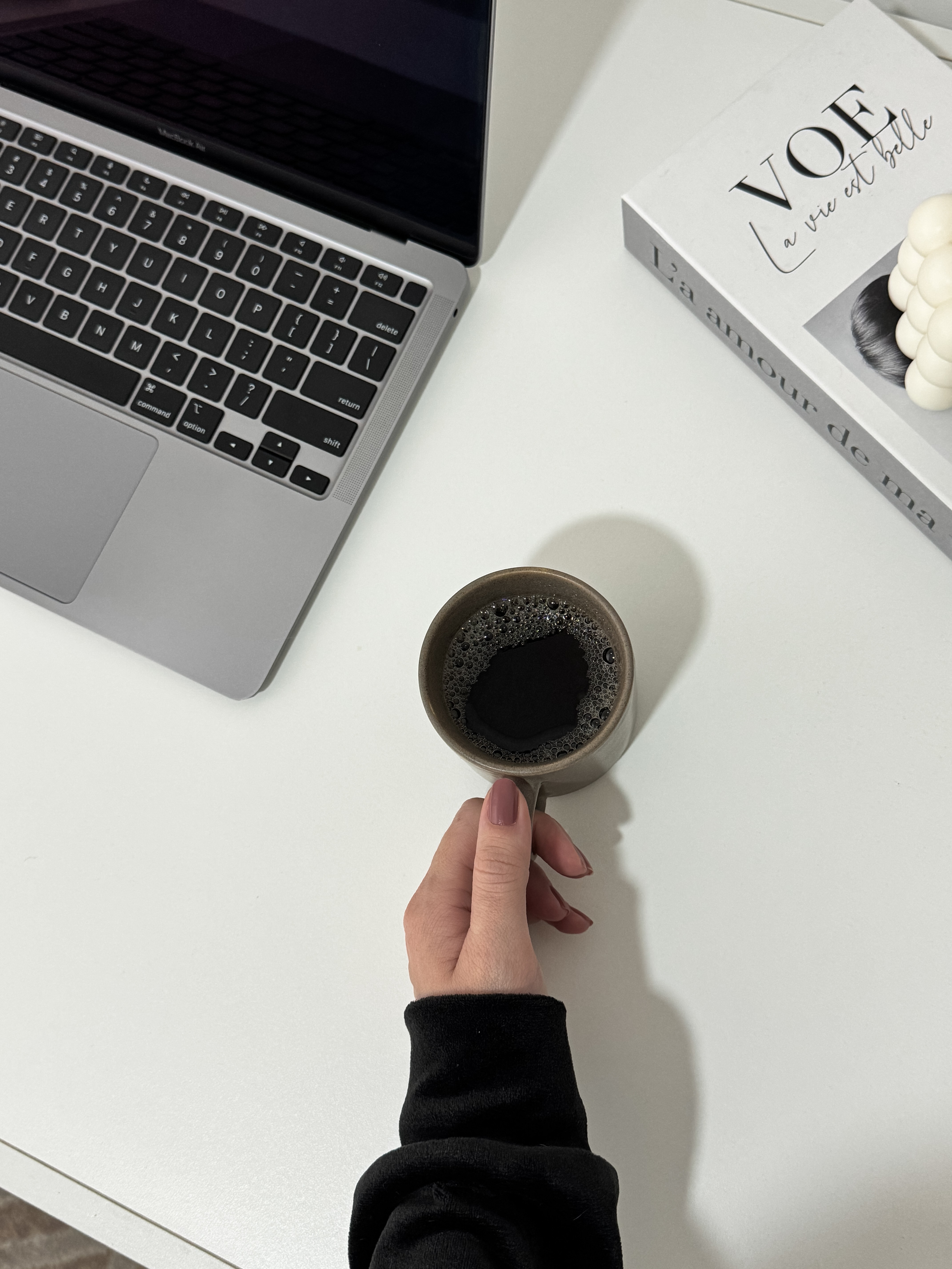 Bird's eye view looking down onto a white desk with a laptop and a hand holding cup of coffee