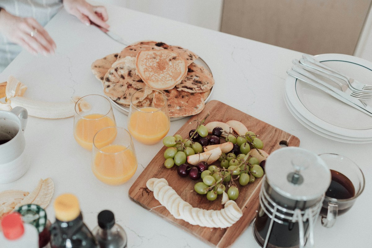 A relaxed table set with plates of food and glasses of juice, reflecting regular, adequate meals and snacks across the day