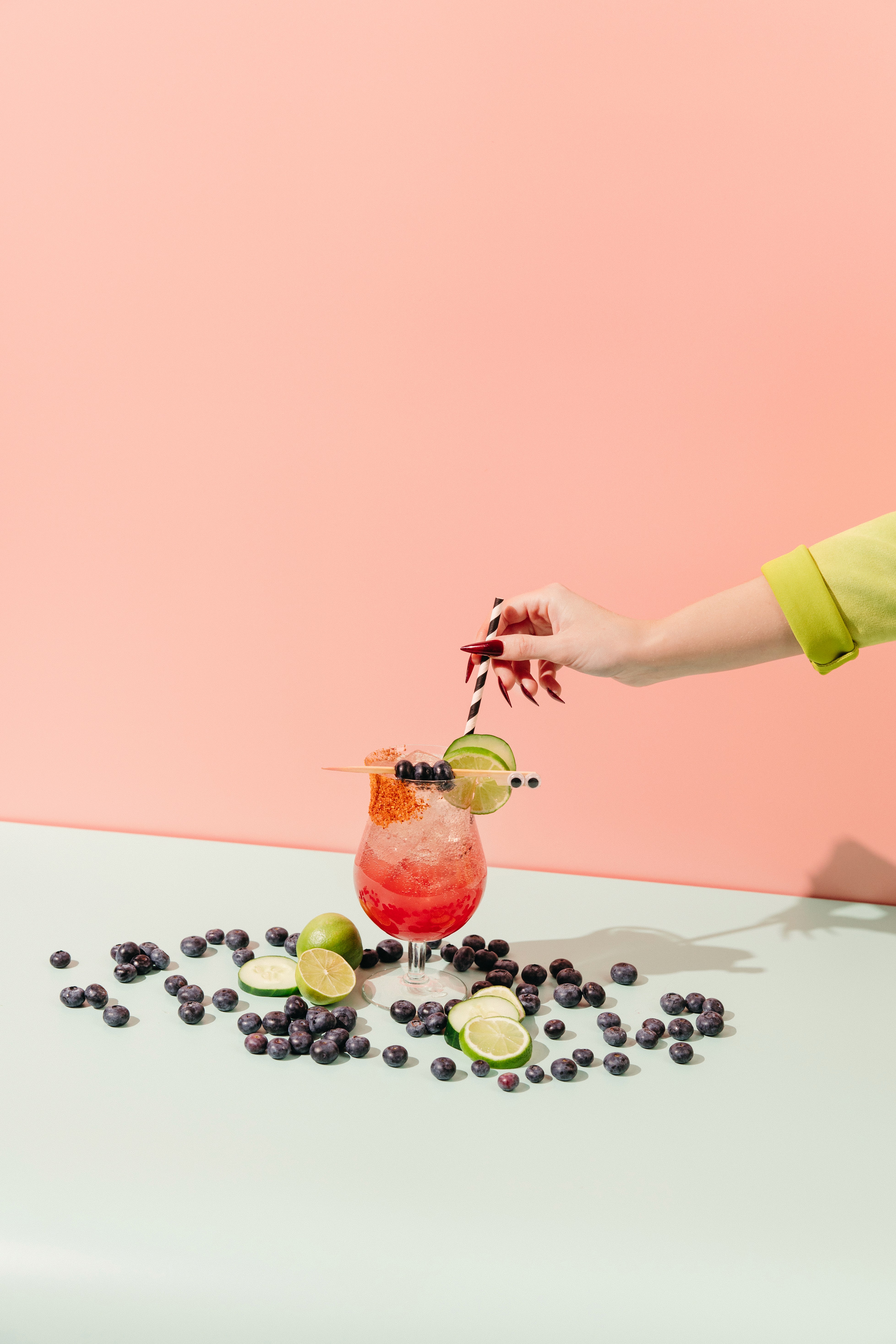 Commercial photography of a vibrant, fruity drink surrounded by blueberries on a pink background