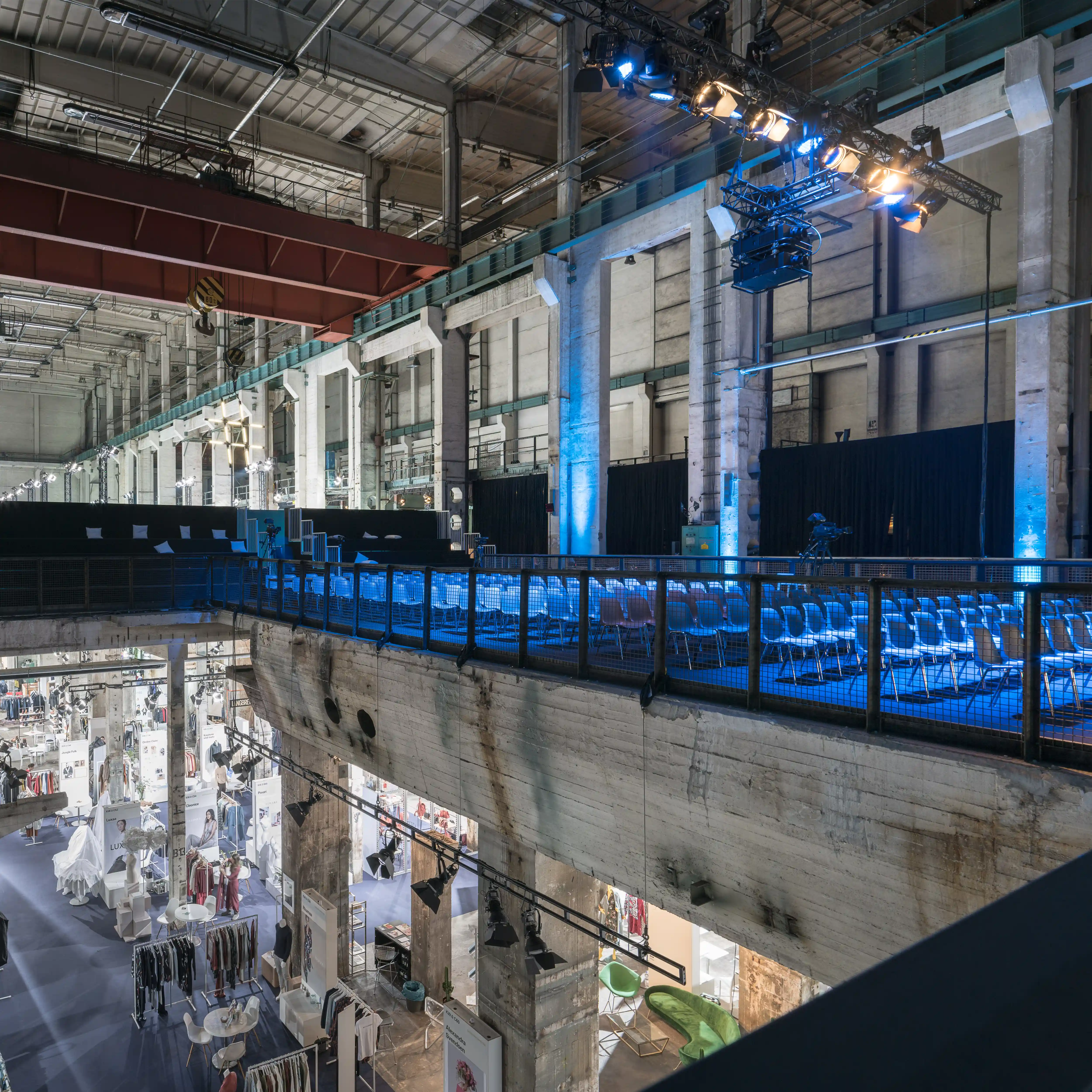Blue-lit conference gallery above the fashion exhibition level at NEONYT, framed by raw concrete pillars and stage rigs.