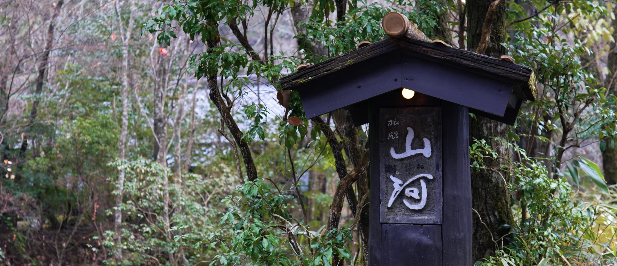 The timber name board of Ryokan Sanga beneath a small tiled roof among trees