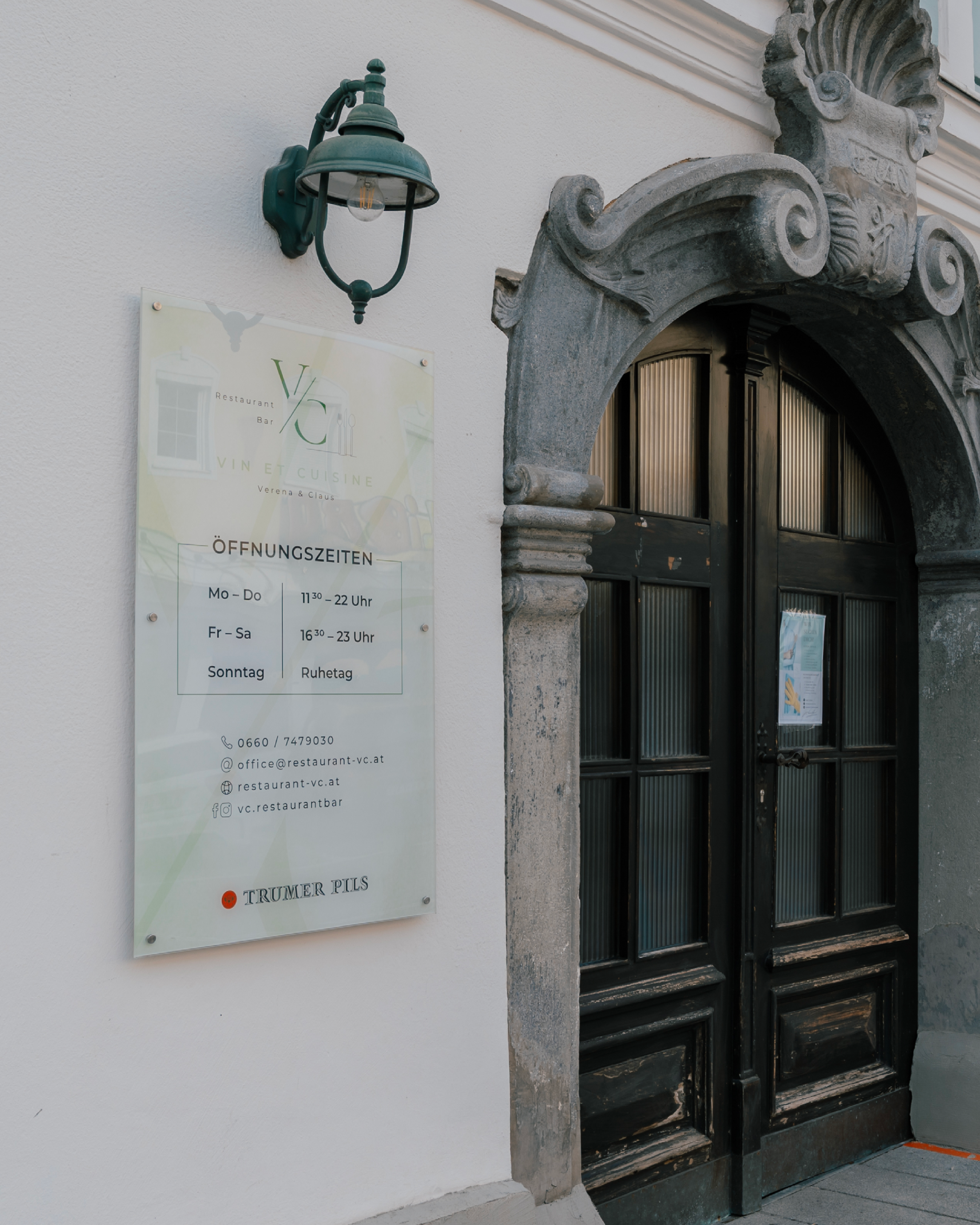 A dark wooden door with a decorative archway next to a light-colored sign mounted on the wall.