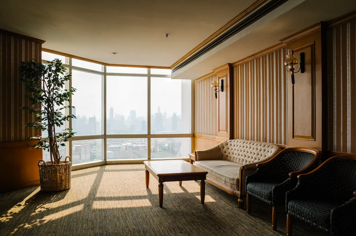 Clifftop Studio — classic lounge room with a curved window wall overlooking the city skyline, tufted sofa and armchairs in warm sunlight