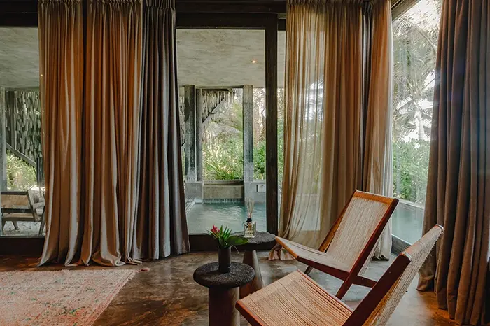 Fuego Suite at Nômade Tulum featuring luxurious finishes and incredible design, comfortable bed with pillows and cushions, 2 hanging lamps in harmony, and huge windows with private pool view.