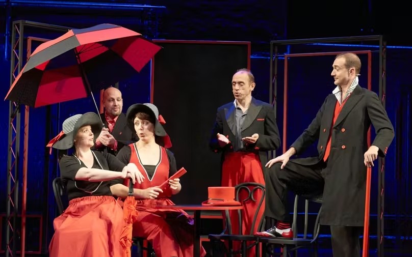 Showstopper! West End cast performing a comedic scene in red and black costumes.