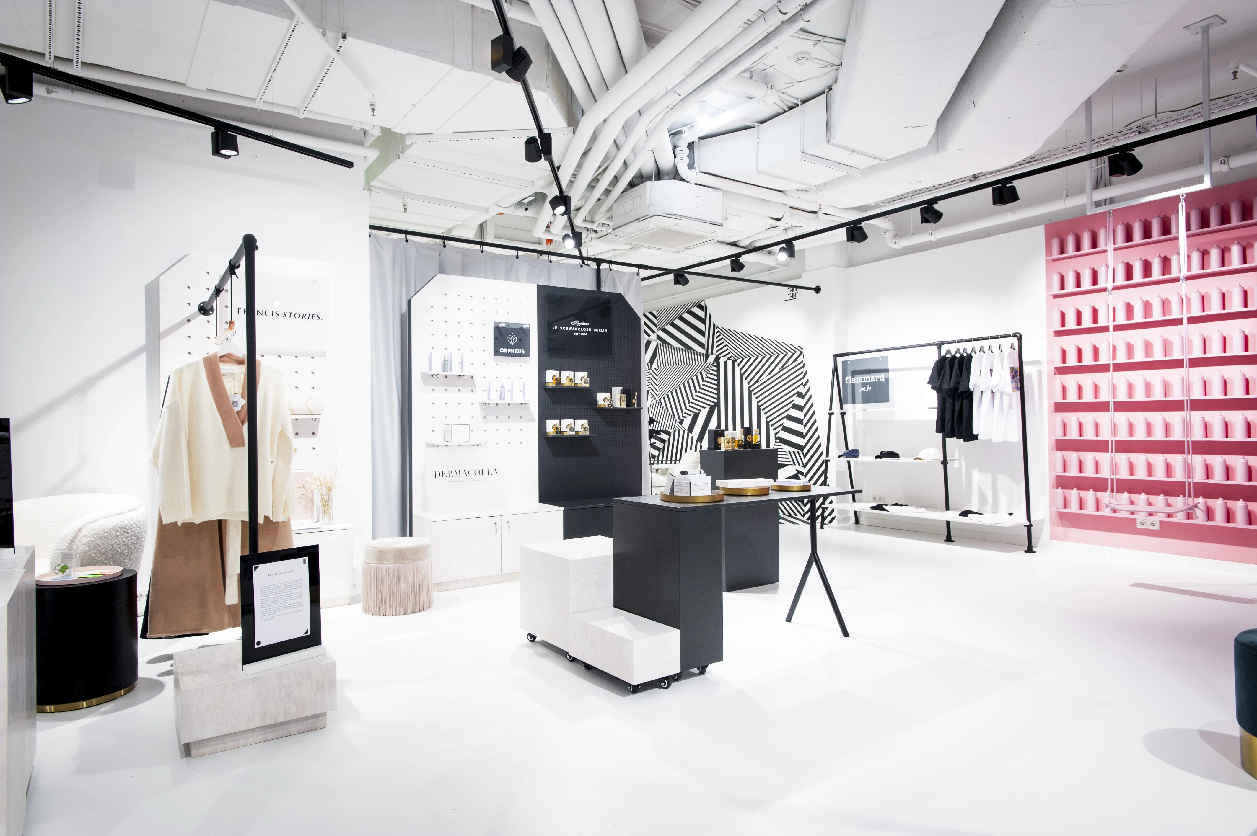 Display area at FREIRAUM SHOP with black product towers and pegboards, cream coats on a rack, a pink shelf wall of spray cans and a dazzle-striped black-and-white corner.