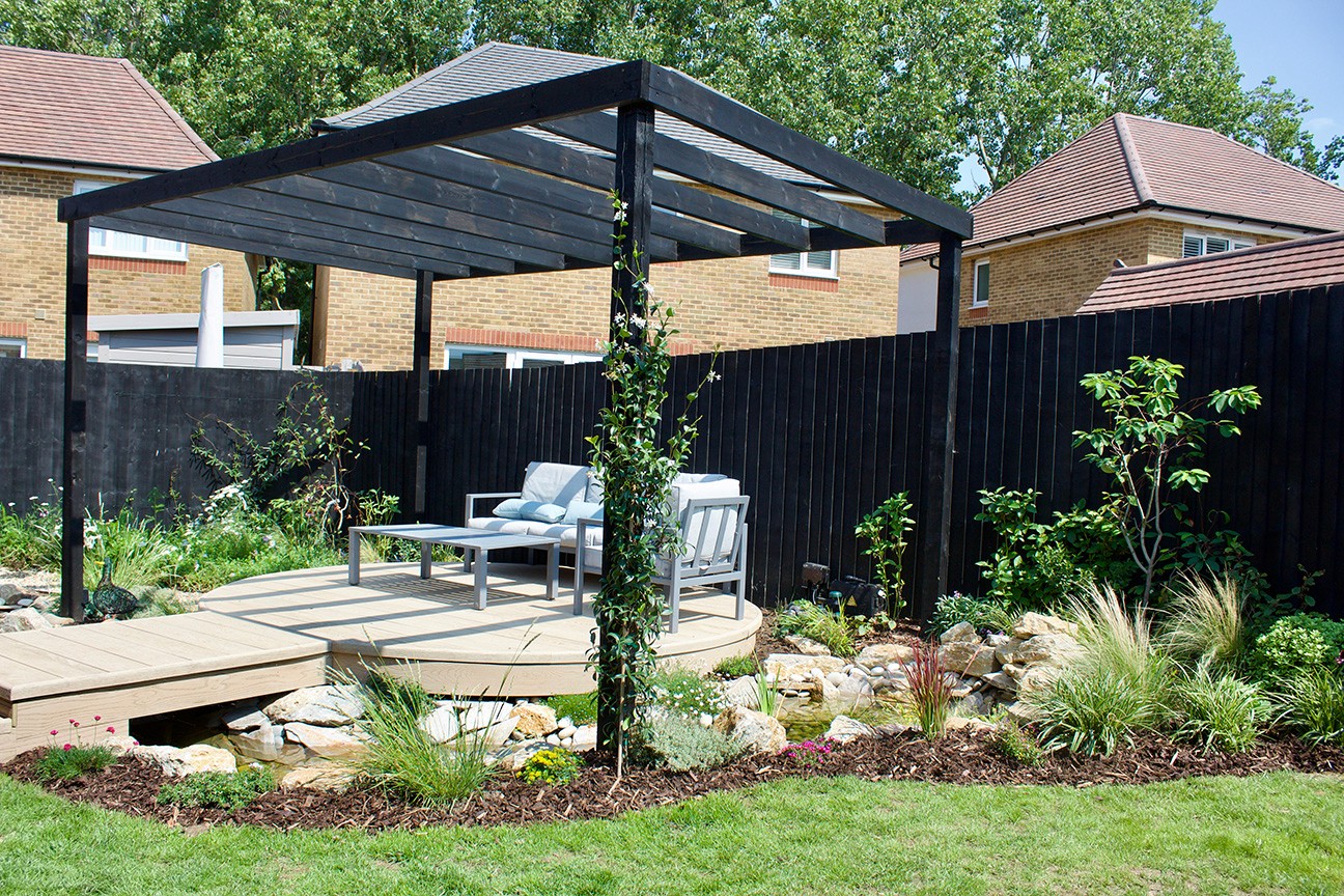 A modern black gazebo in a landscaped yard, surrounded by greenery and a stone path.