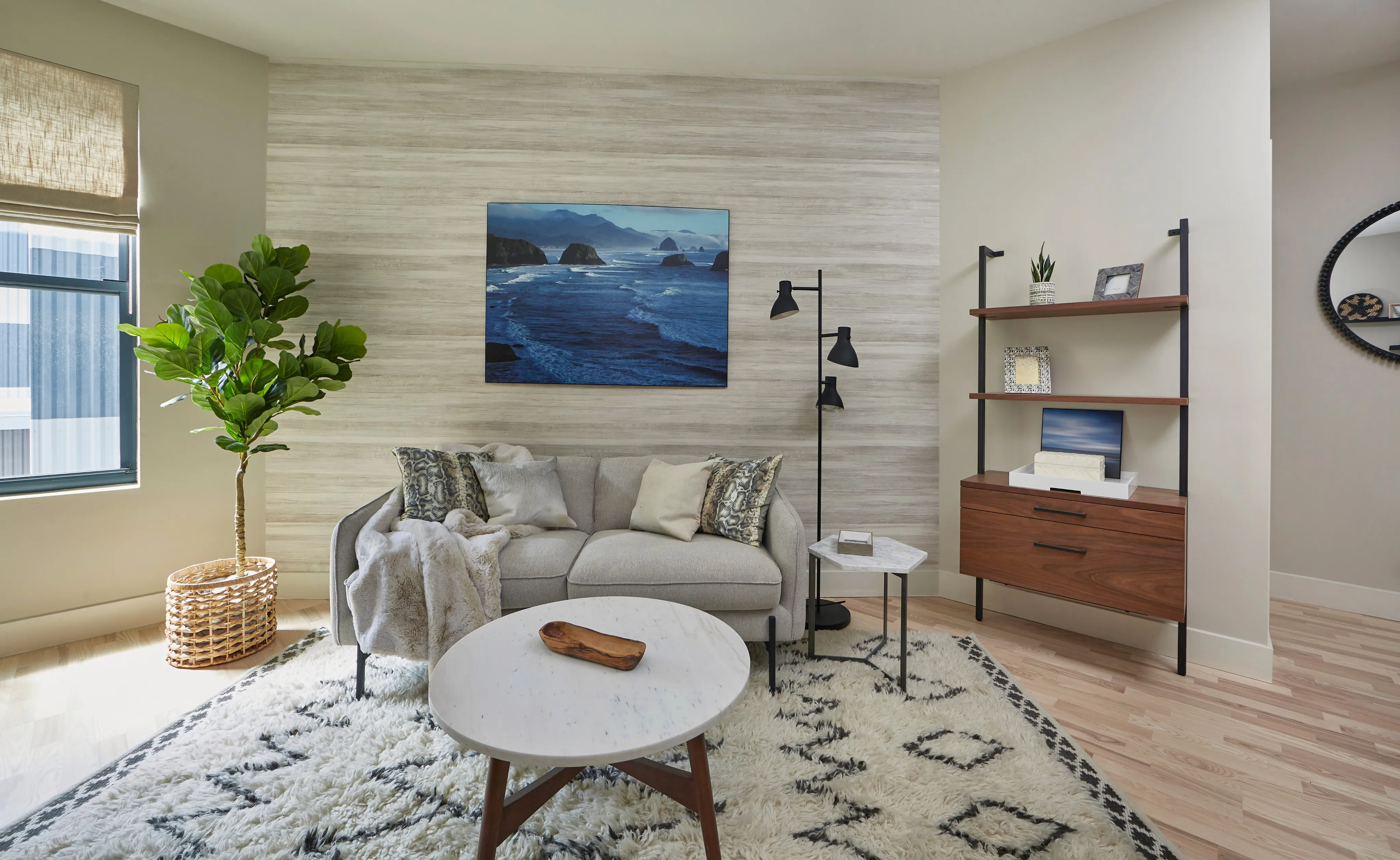 Bright living room featuring a gray sofa, decorative plants, a round coffee table, and a shelf with books.