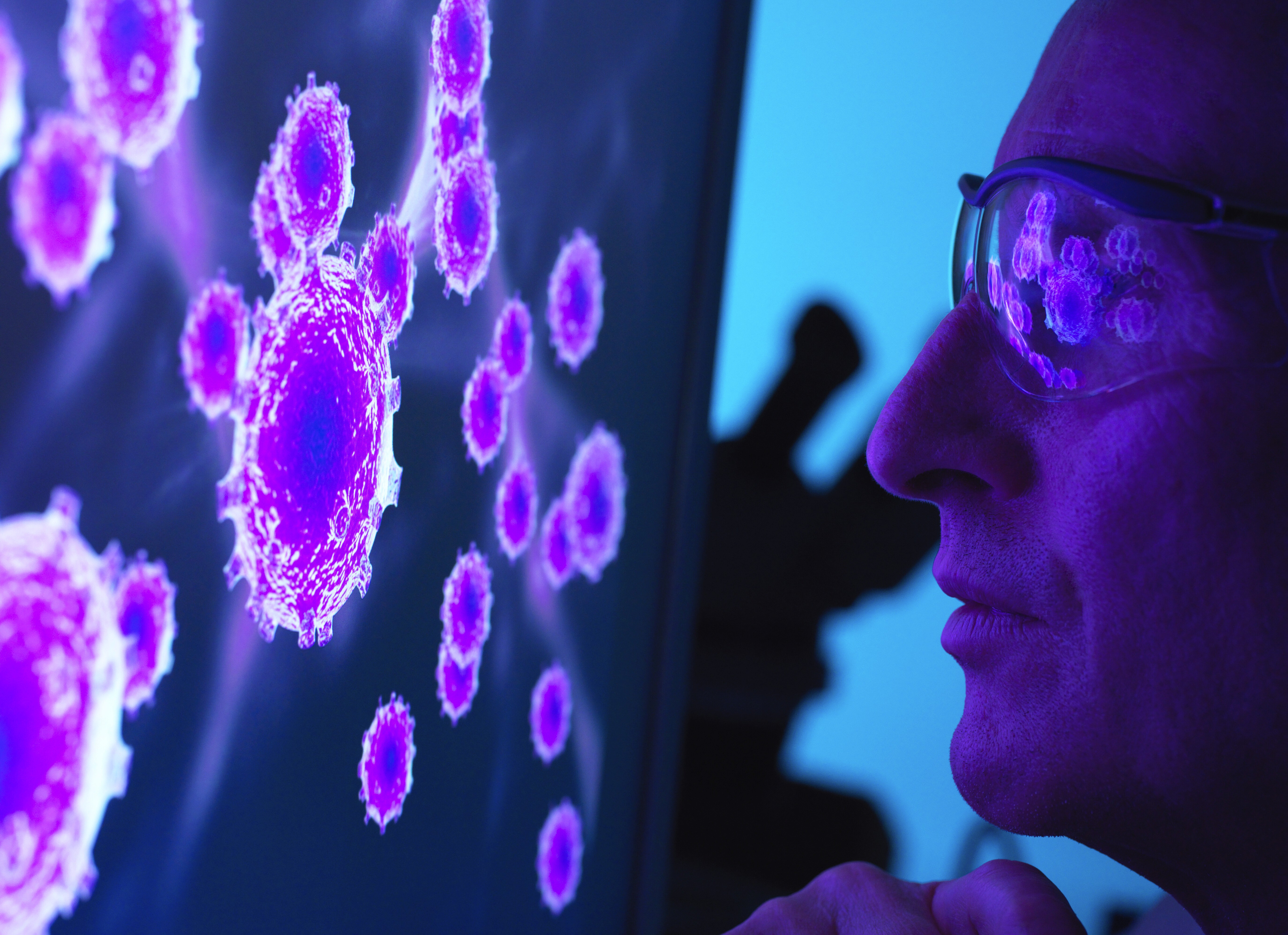 A man in a white lab coat working at a computer, viewing a 3D model on the screen in a laboratory or office setting.