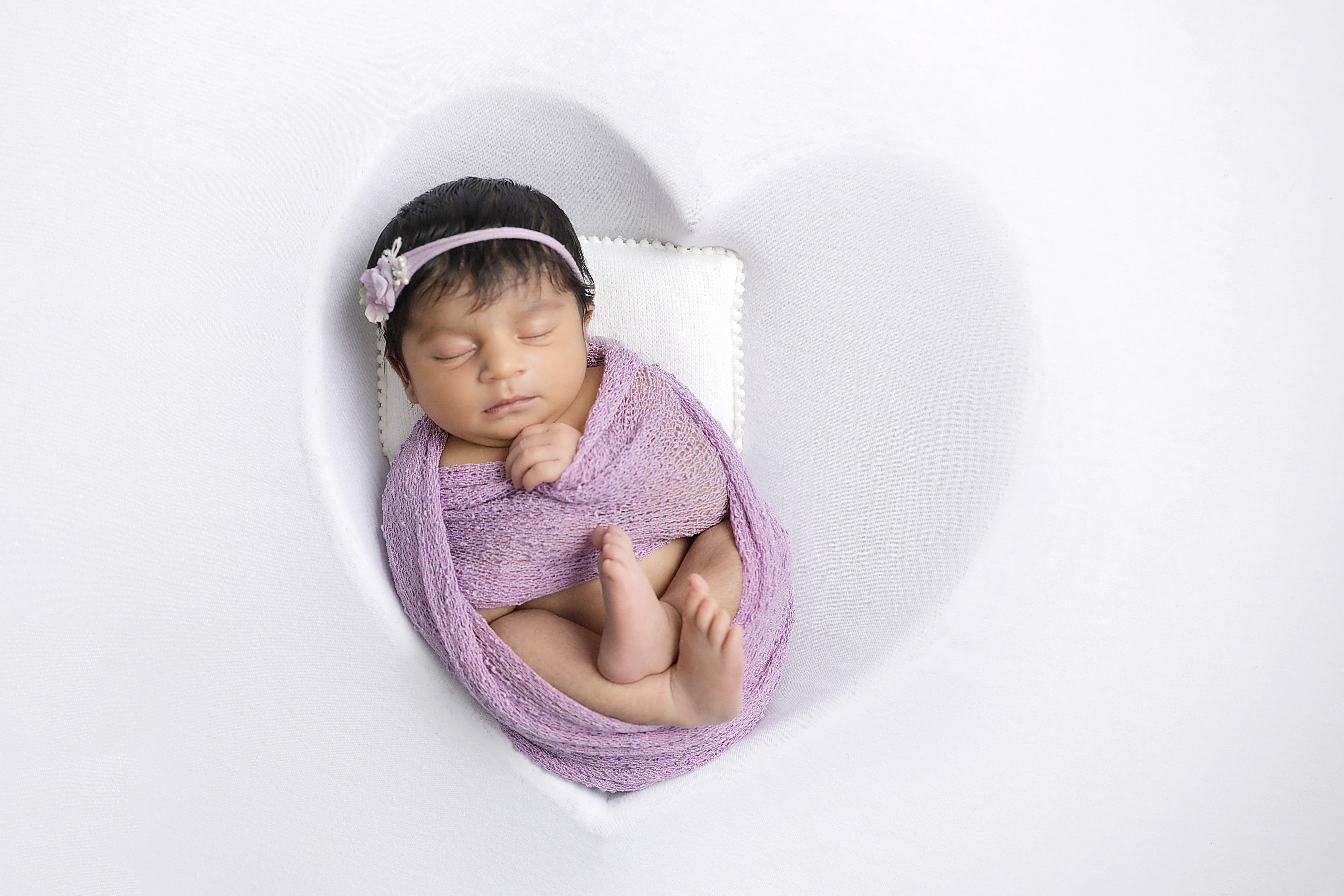 Baby in a purple swaddle for newborn photoshoot.