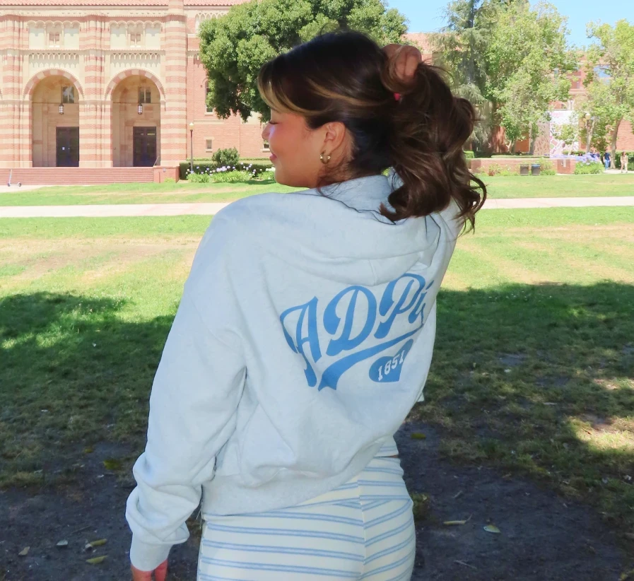 Clarissa, posing outdoors in a soft light gray sorority sweatshirt with ADPI printed on the back.