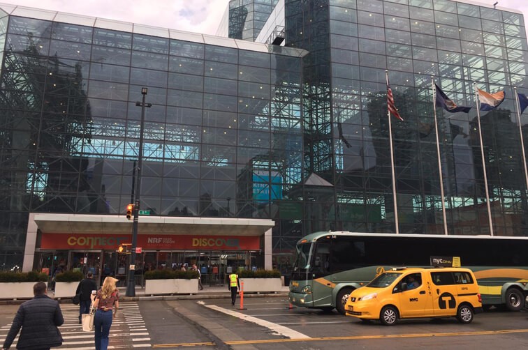 Exhibition center entrance with people, taxi, and bus outside