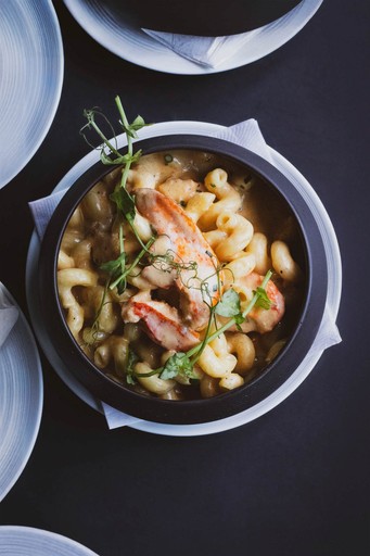 Overhead view of a bowl of lobster mac and cheese. The pasta is creamy and topped with lobster meat and pea shoots.