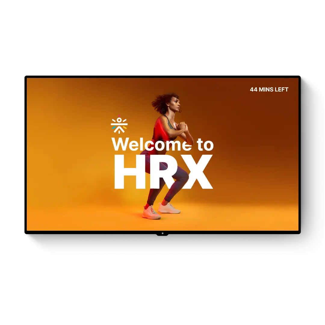 Digital screen displaying ‘Welcome to HRX’ with a person performing a squat against an orange background, with gym equipment like kettlebells and gloves in the foreground.