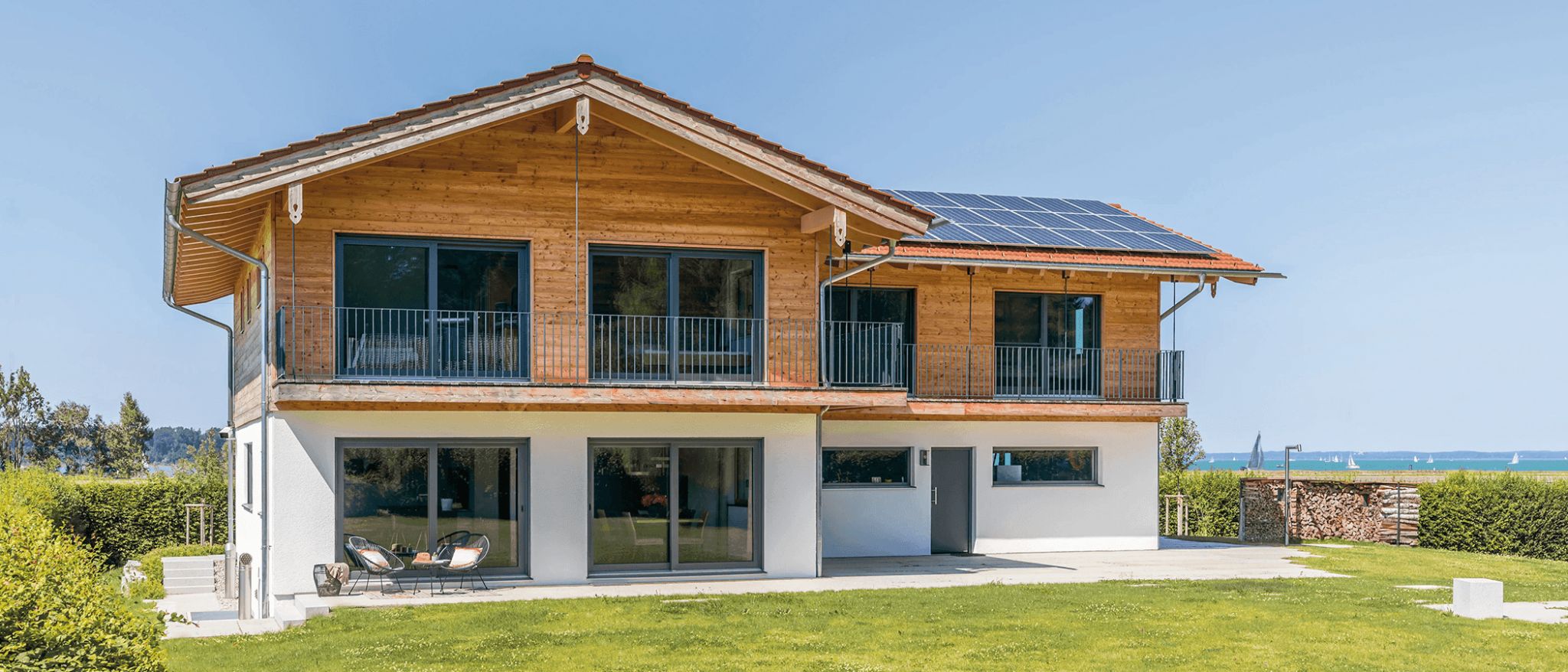 Modernes Haus mit Holzfassade, Balkonen, Bodentiefen Fenstern und Solaranlage auf dem Dach.