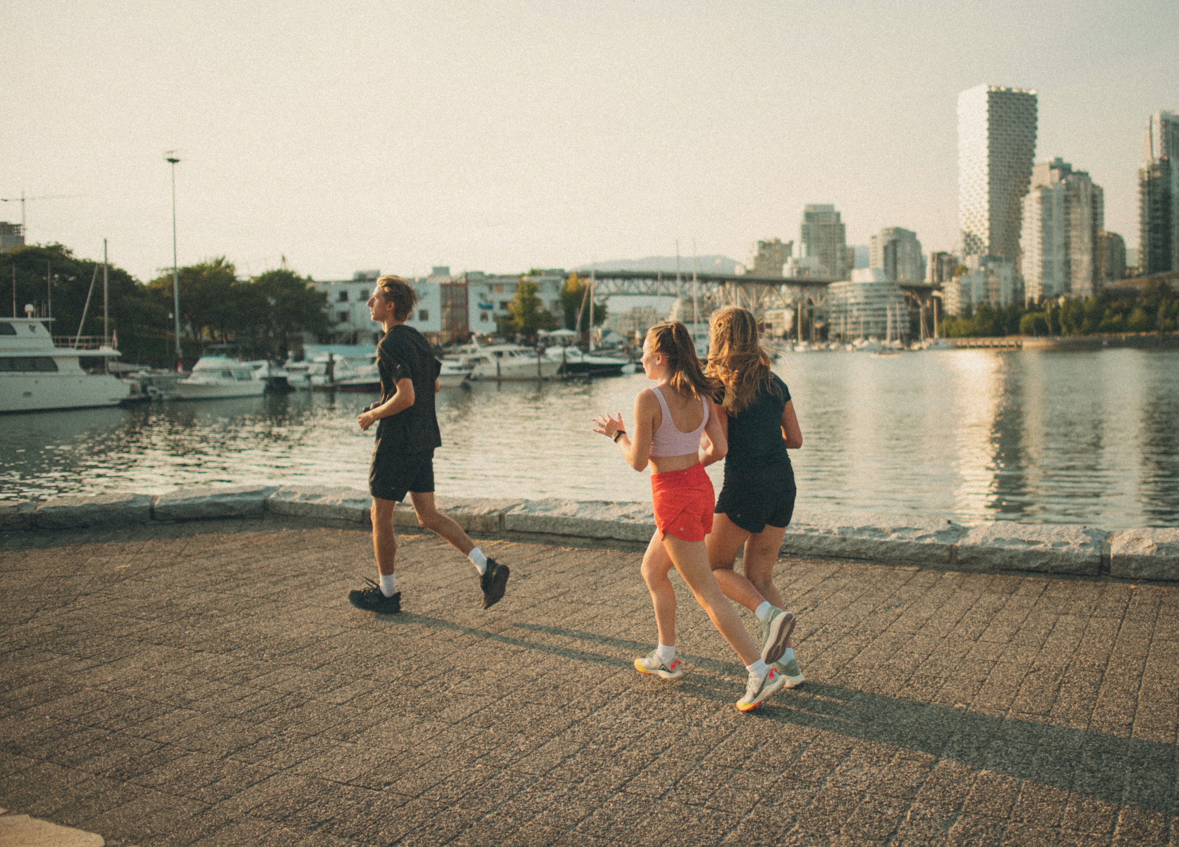 Three women in athletic wear smiling and linking arms outdoors under a bright blue sky, each wearing Pyra-branded sports apparel and visors or caps.