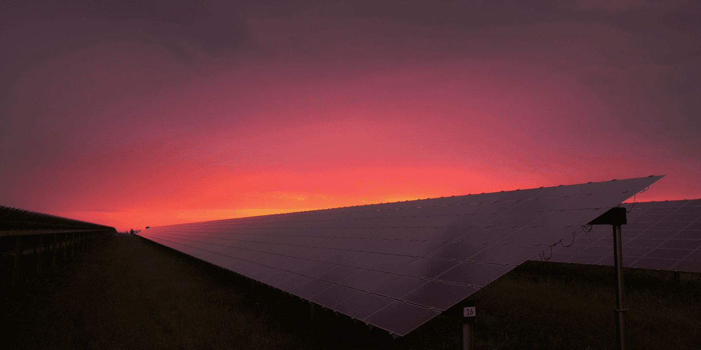Large solar photovoltaic array stretching into the distance under a red-orange sunset.