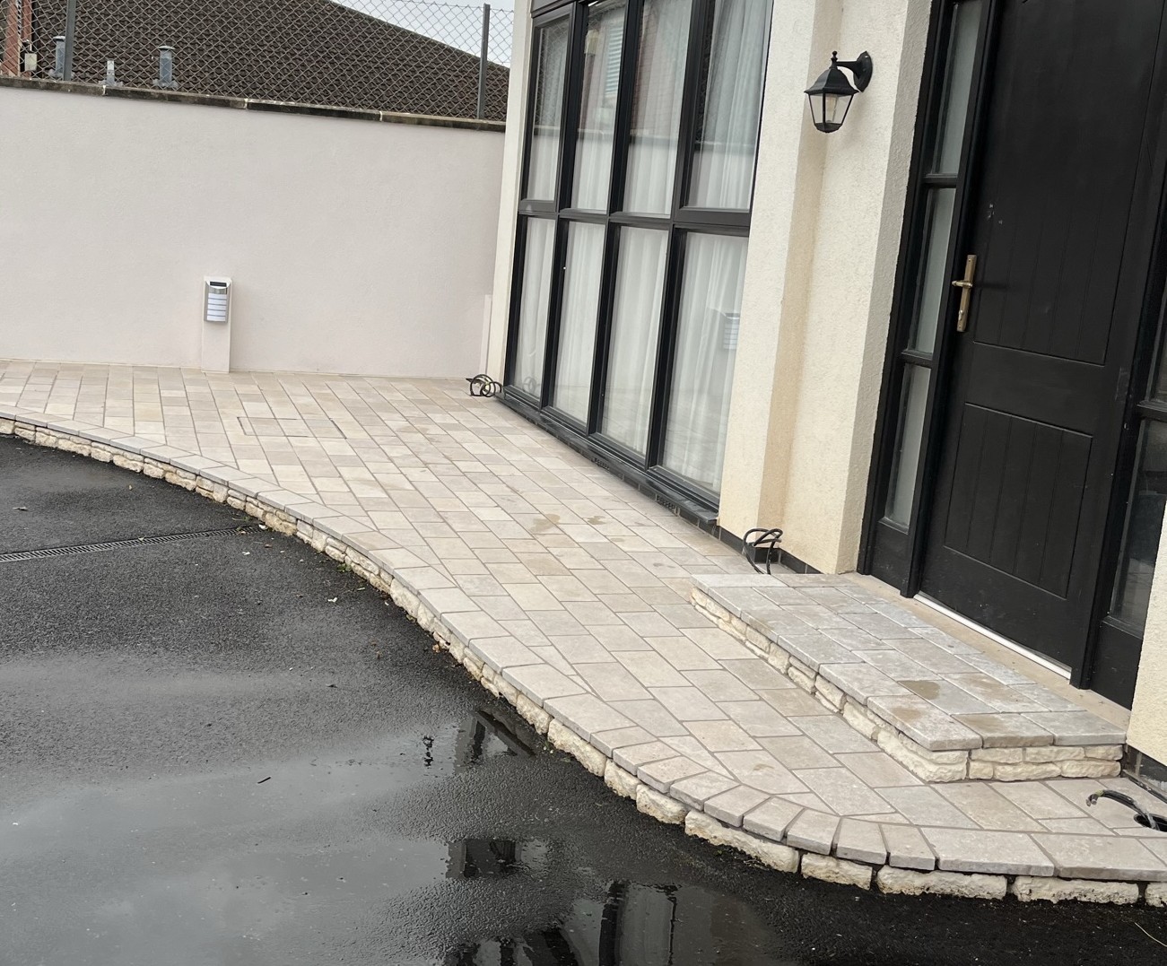 Curved pale block paving fitted around the outside of a house beside dark ground.