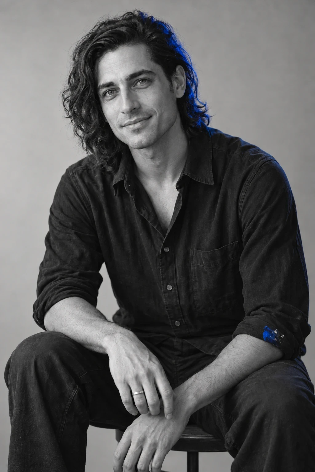Selective-colour version: Elio, D’CALOR colour artist, seated in a black shirt with wavy shoulder-length hair