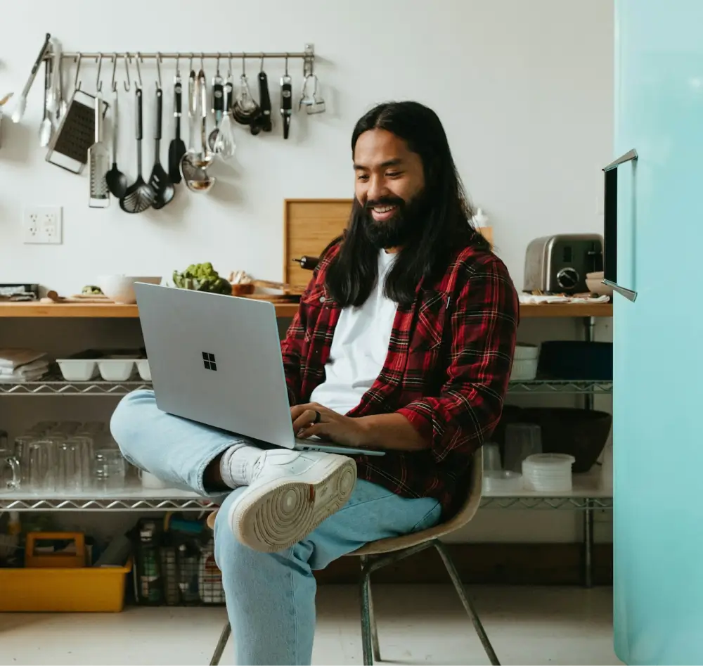 Photograph of man sitting, smiling while using a laptop 