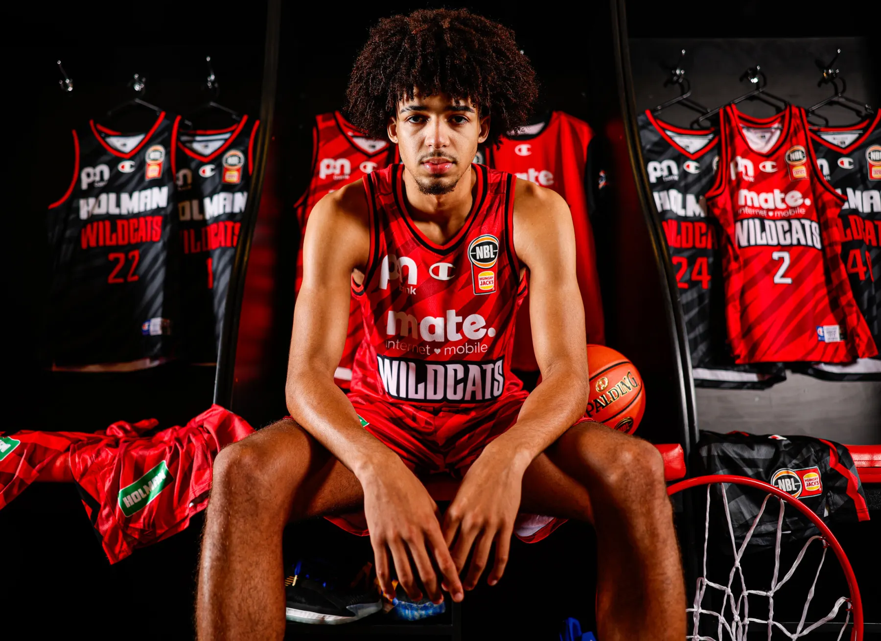Perth Wildcats player seated in front of the redesigned home and away jerseys