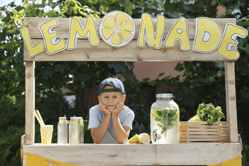 Child resting chin on hands at a lemonade stand with jars of lemonade and lemons.