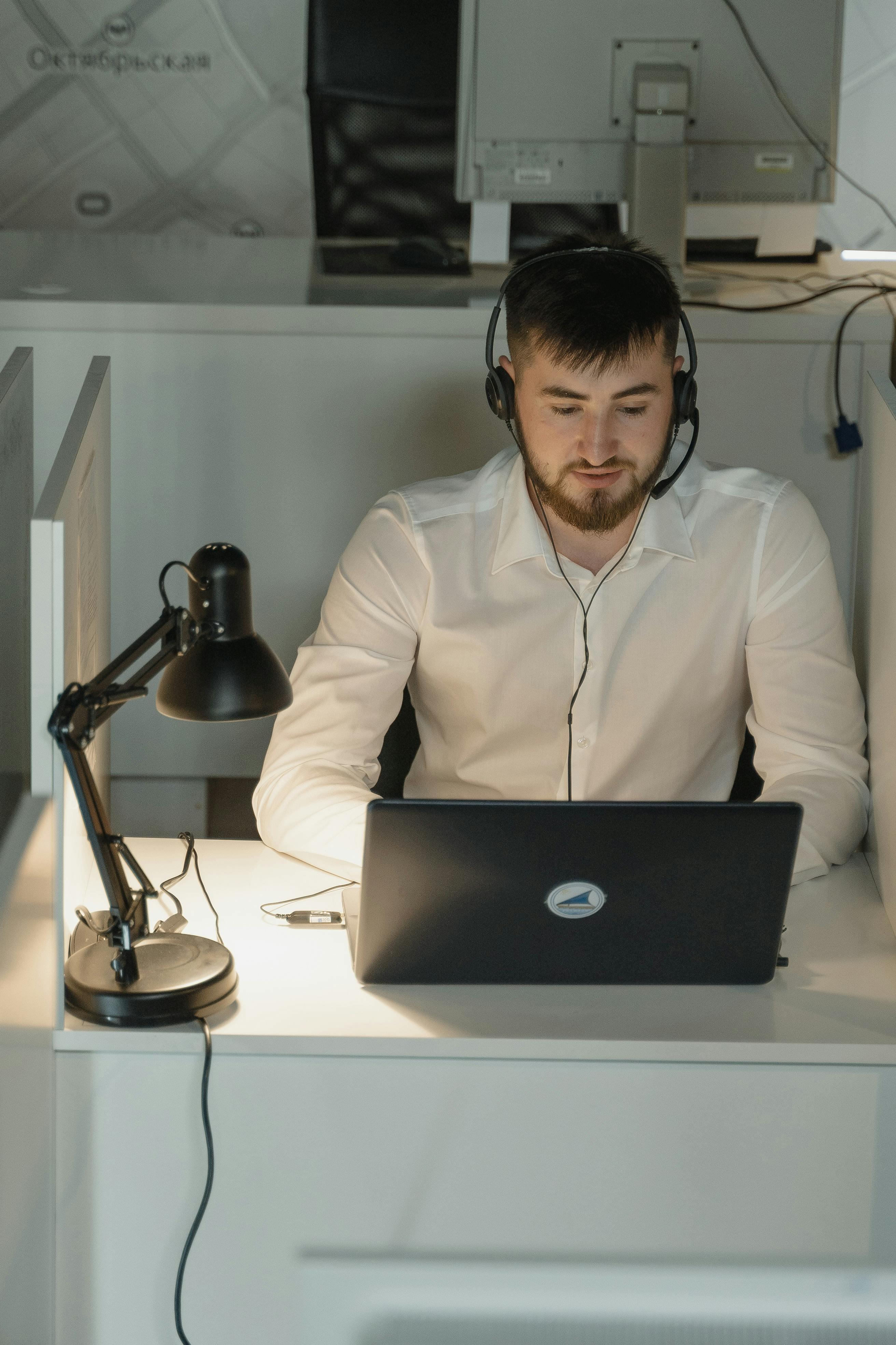IT support specialist wearing a headset while working on a laptop in a modern office.