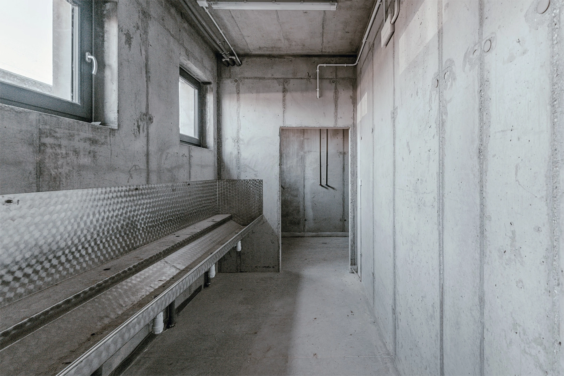 Korytarz z betonowymi ścianami i drzwiami po obu stronach. Widok z perspektywy w głąb korytarza.