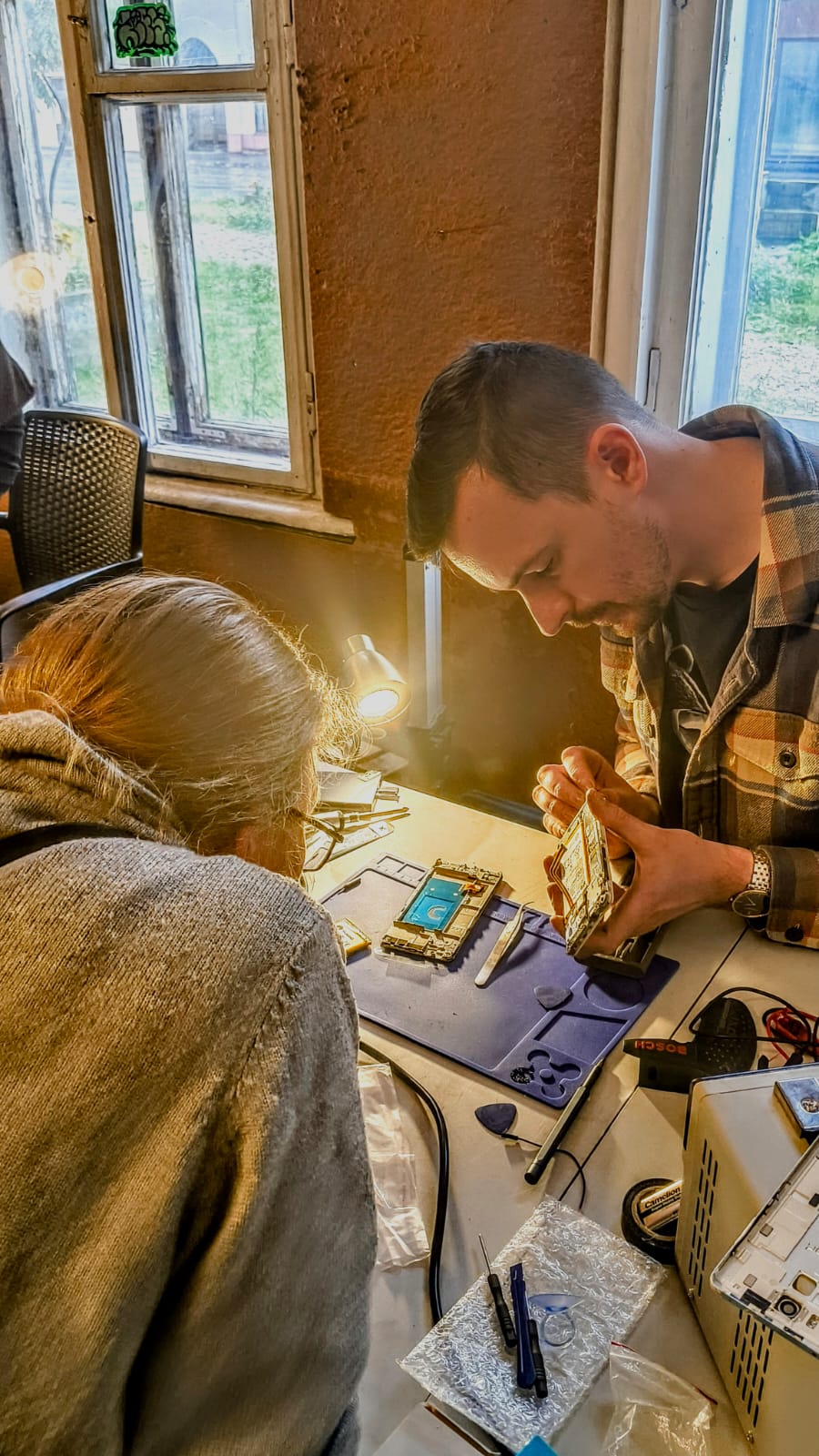 A volunteer repairs a visitor's phone, the kind of small, social fix that REBOOT is designed around.