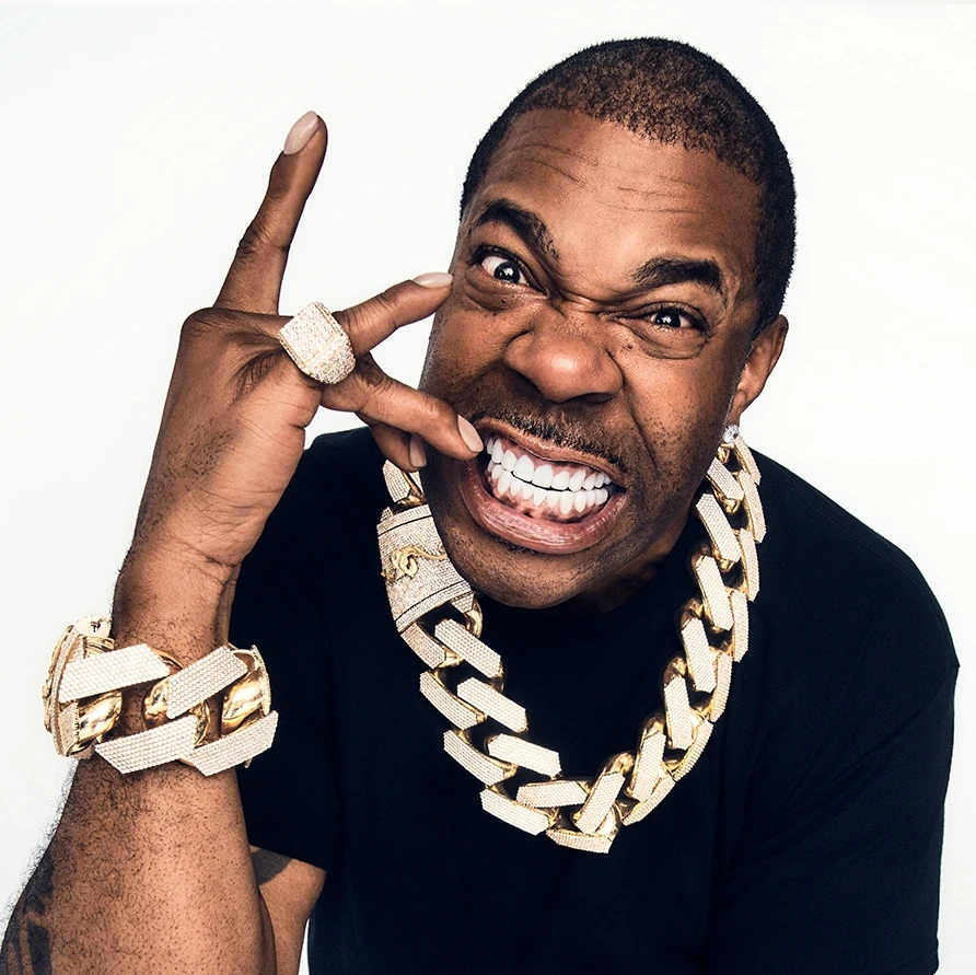 A person with a cheerful expression is making a hand gesture while wearing a large chain necklace.