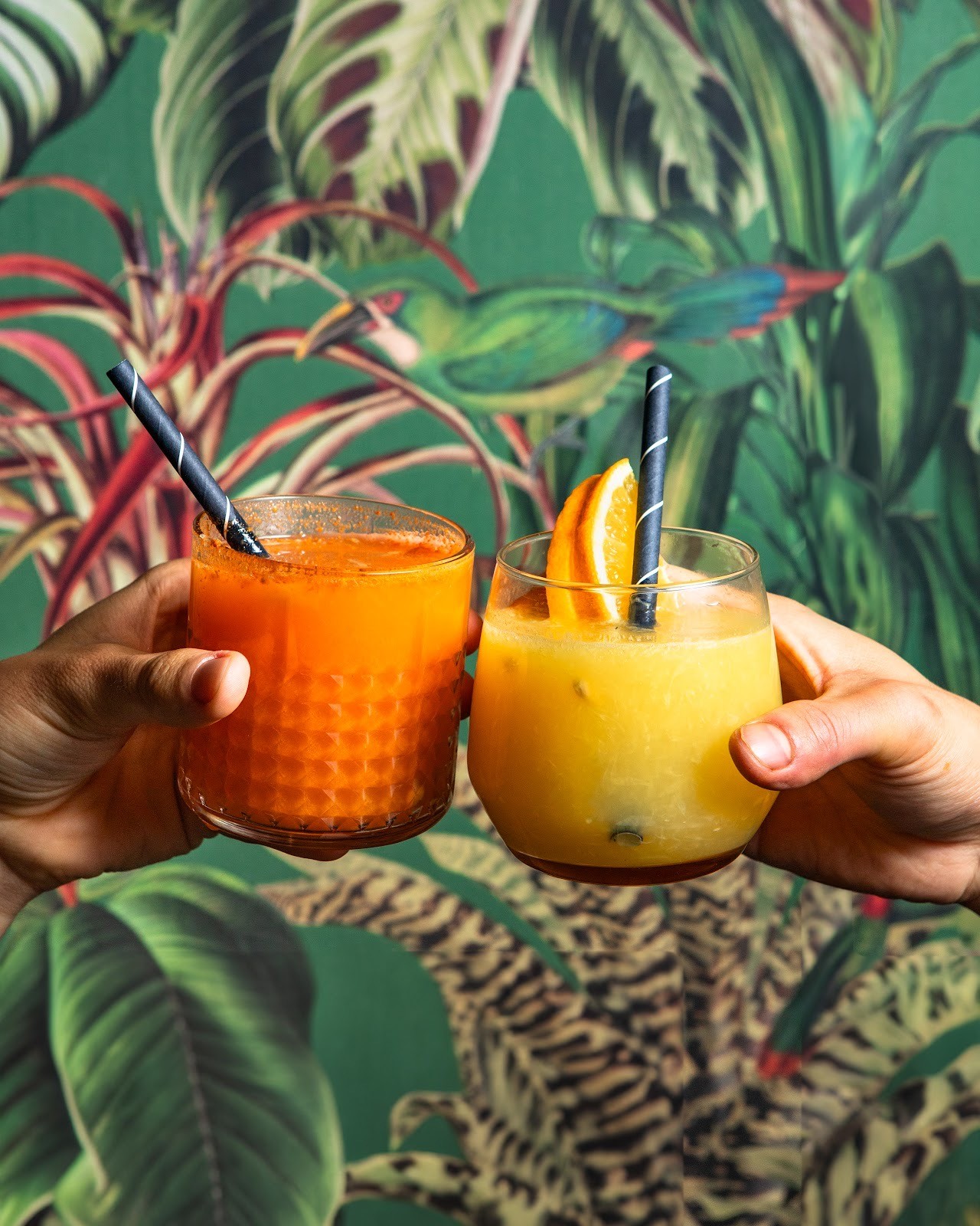 Ein erfrischender Orangensaft in einem hohen Glas, garniert mit einer Orangenscheibe und einer roten Beere, auf einem roten Tisch.