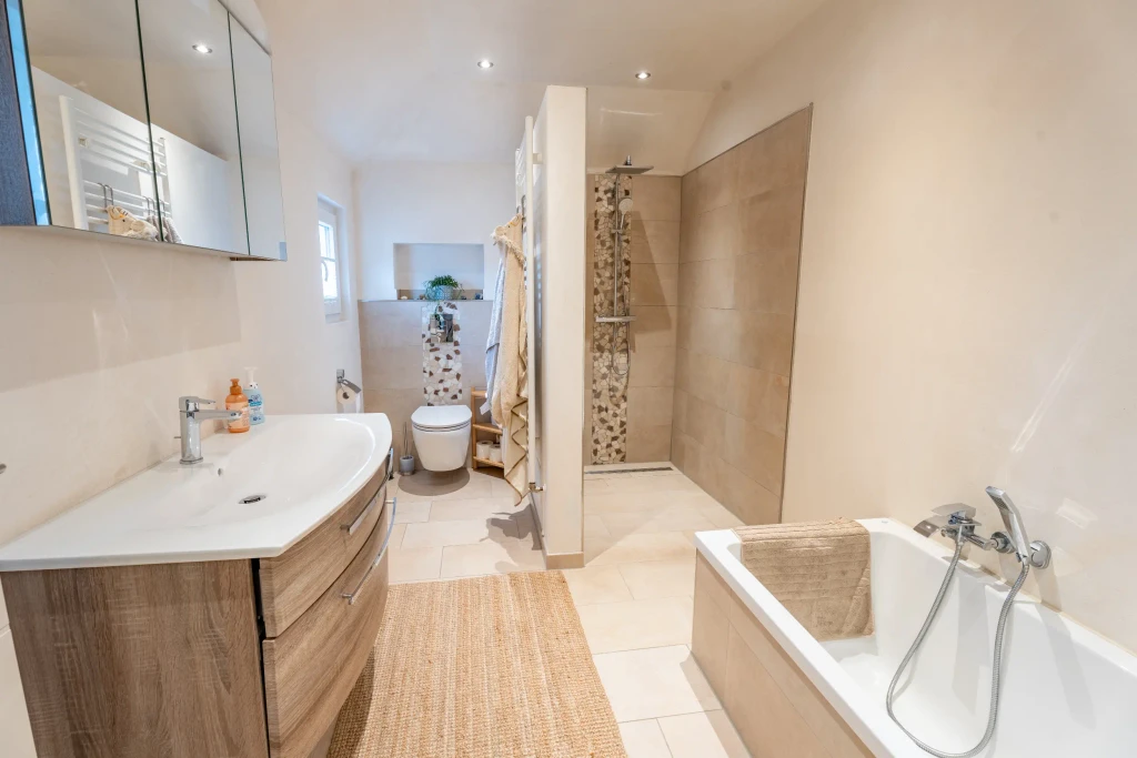 Modernes Badezimmer mit bodengleicher Dusche, Badewanne und Holzwaschtisch in einem Einfamilienhaus in Gronau – Westfalen Wohnen.