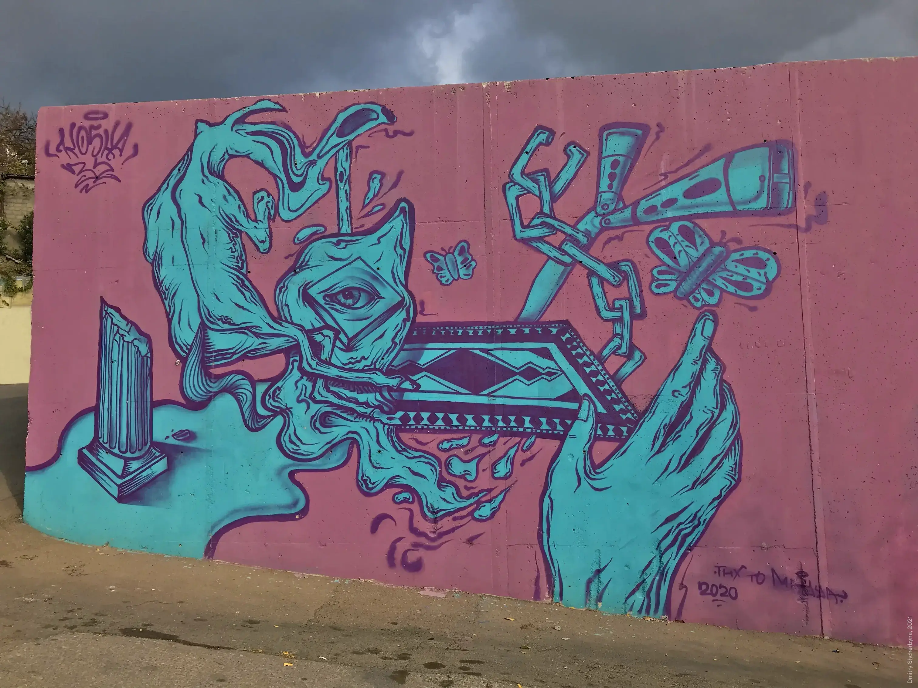 A teal-on-pink mural with surreal imagery, including two large hands forming a heart around a single eye and reaching toward butterflies and a megaphone, floats in the center. A geometric carpet pattern is on the floor, with a classical column on the left side.