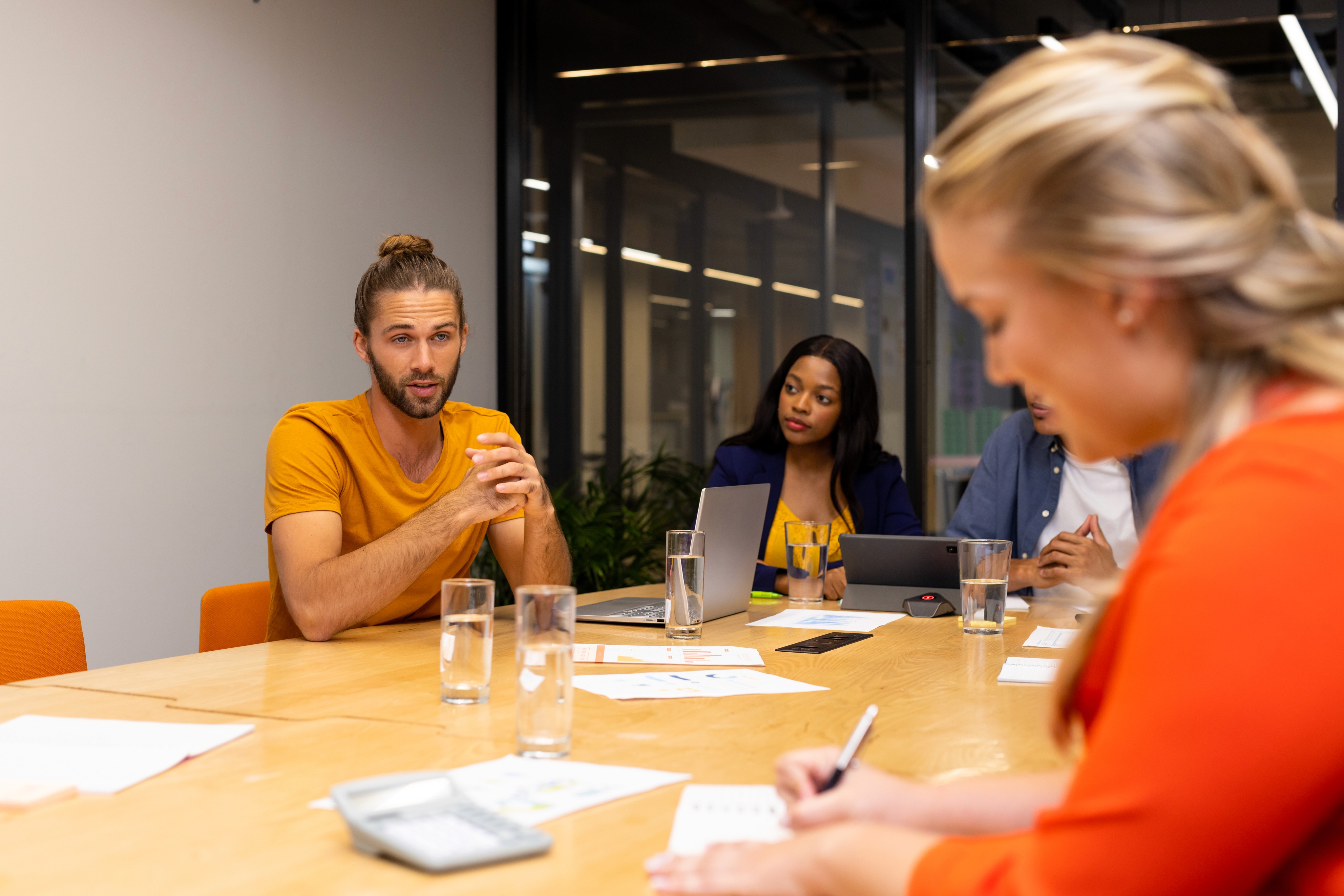 Team meeting with a man speaking while colleagues listen and take notes around a conference table.