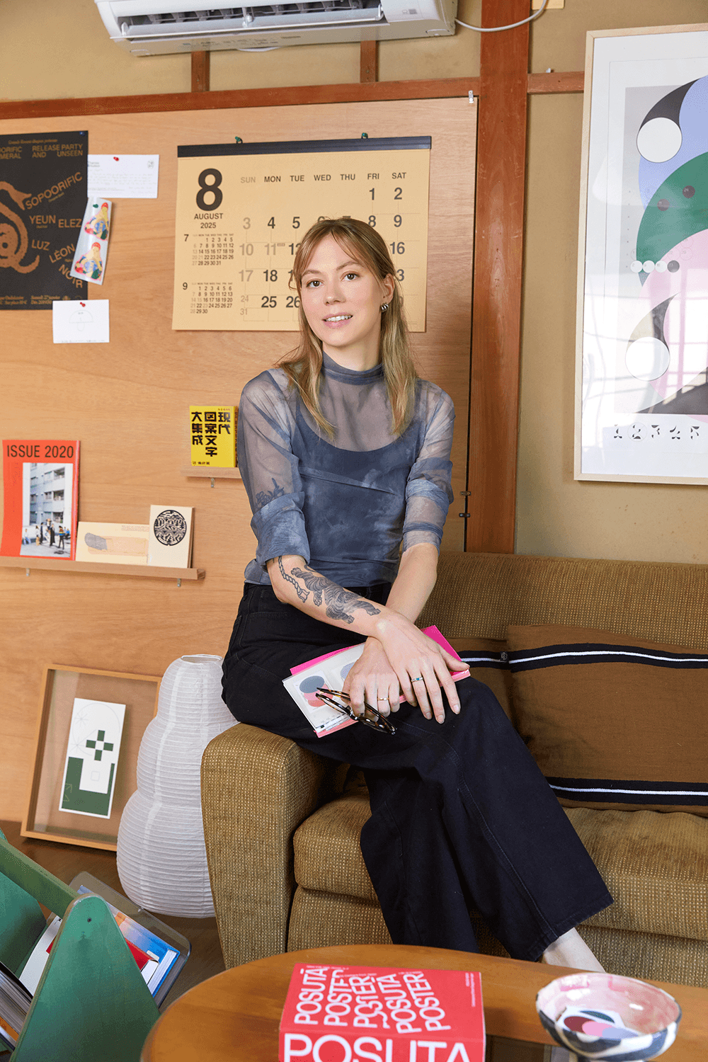 A designer sitting in a design studio, holding a notebook, surrounded by posters, books and Japanese interior details.